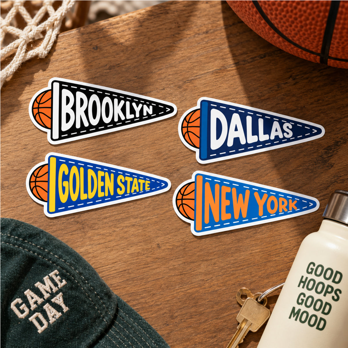 Basketball-themed pennant stickers reading arranged on a wooden tabletop with a basketball, hat, keys, and bottle nearby.