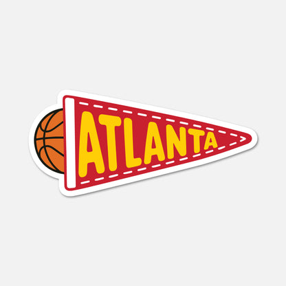 A die-cut sticker shaped like a red football-style pennant with the word ATLANTA in large yellow letters, plus a small basketball peeking out from the left, shown on a light gray background.