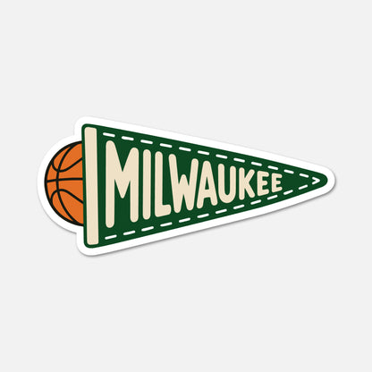 A die-cut sticker featuring a green triangular pennant with the word 'MILWAUKEE' in cream lettering, a basketball peeking out from behind the left edge, and a white border, shown on a light gray background.