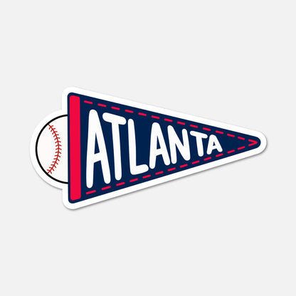 A die-cut sticker shaped like a navy blue pennant with red trim and white lettering that says ATLANTA, with a baseball partially visible behind the left side on a light gray background.