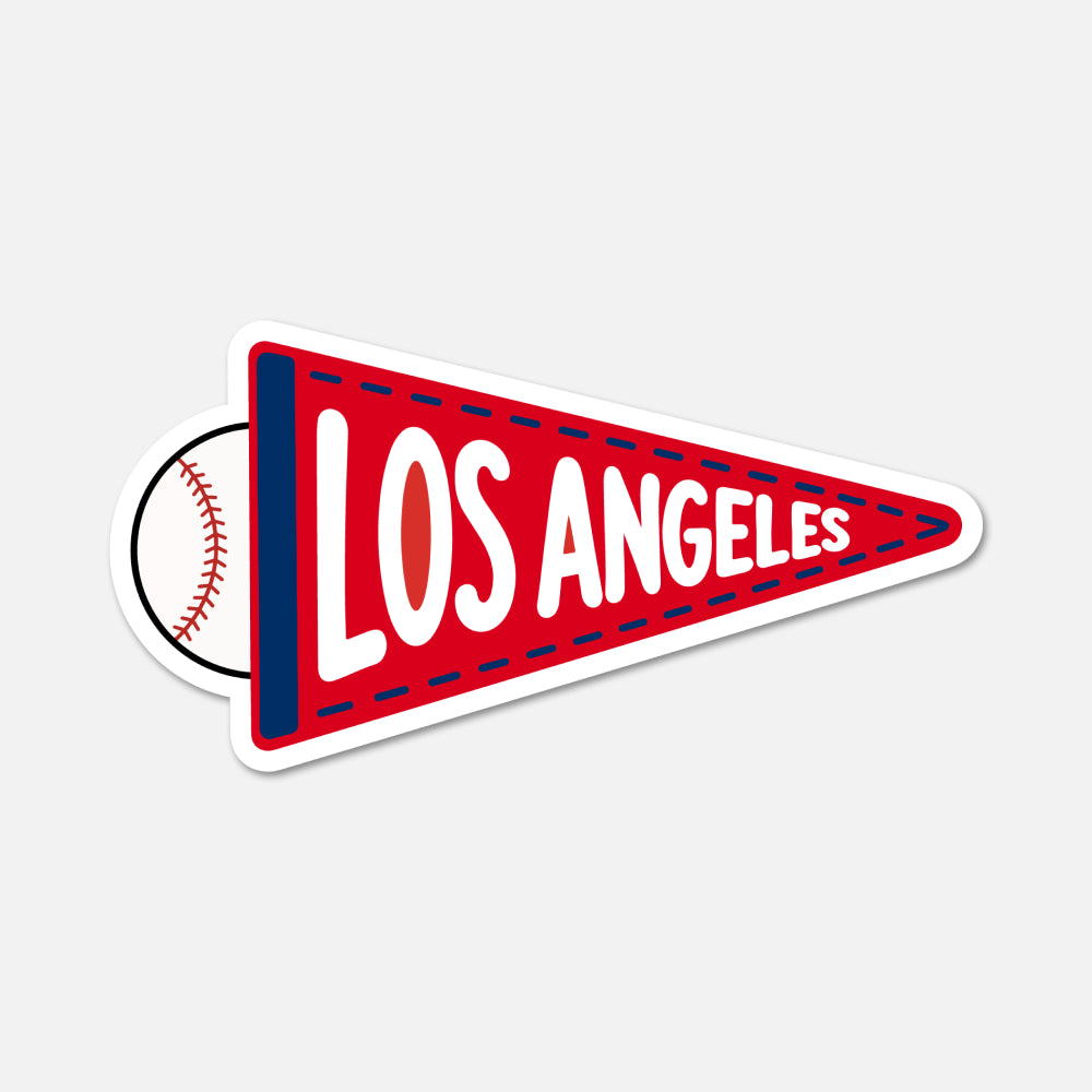 A die-cut sticker shaped like a red Los Angeles sports pennant, featuring white 'LOS ANGELES' text, a navy vertical stripe, dashed stitching details, and a baseball graphic peeking out from behind on the left, shown on a light gray background.