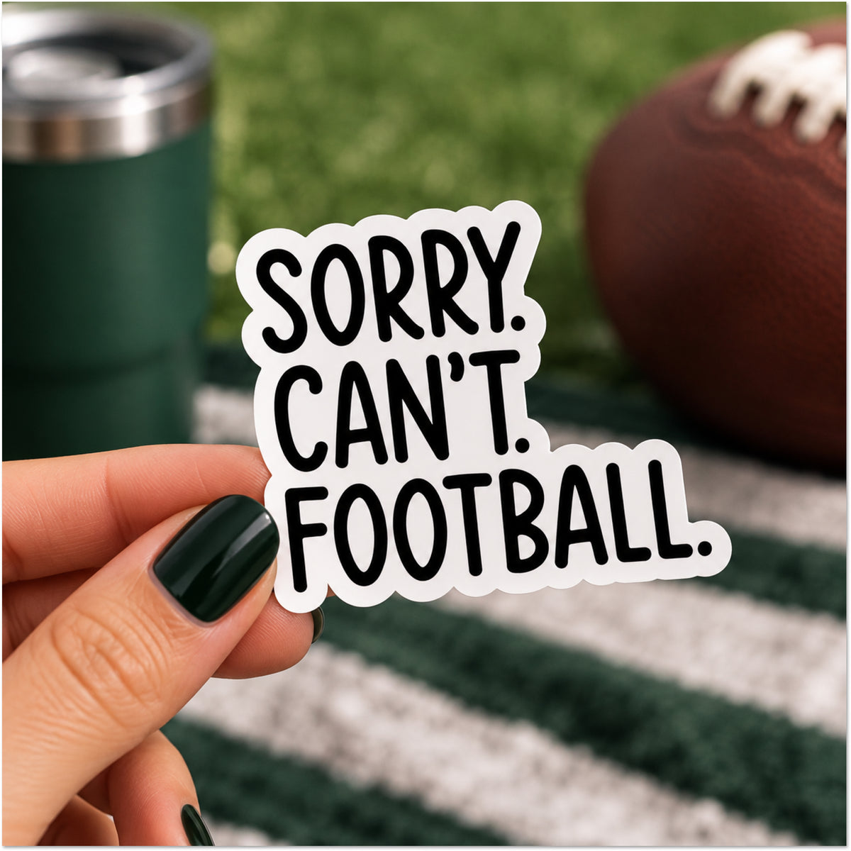 A hand with dark green nail polish holds a die-cut vinyl sticker that reads 'SORRY. CAN'T. FOOTBALL.'