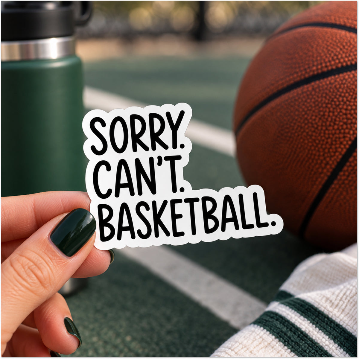 A hand with dark green nail polish holds a die-cut sticker that reads 'SORRY. CAN'T. BASKETBALL.'