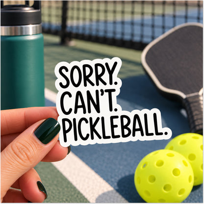 A hand with dark green nail polish holds a die-cut sticker that reads 'SORRY. CAN'T. PICKLEBALL.'