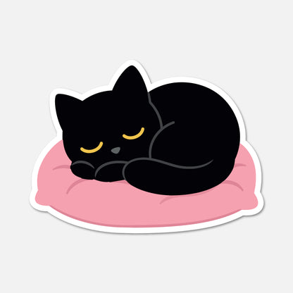 A die-cut sticker featuring a cartoon illustration of a sleeping black cat curled up on a pink cushion, shown on a light gray background.