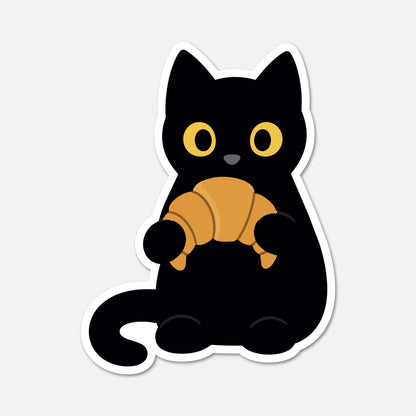 A die-cut sticker featuring a cartoon black cat holding a golden-brown croissant, shown on a light gray background.