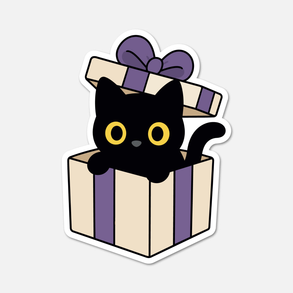 A die-cut sticker featuring a cute cartoon illustration of a black cat with yellow eyes popping out of a cream and purple gift box with a matching bow, shown on a light gray background.