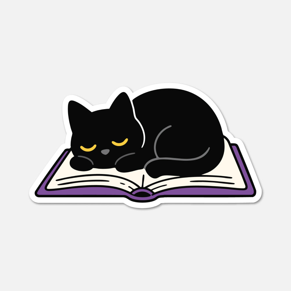 A die-cut sticker featuring a cartoon black cat curled up asleep on an open book with purple pages and a white border, shown on a light gray background.